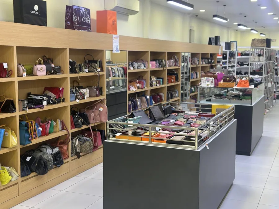 Aisle of shelved handbags and a wallet display case, including Chanel and Gucci packaging